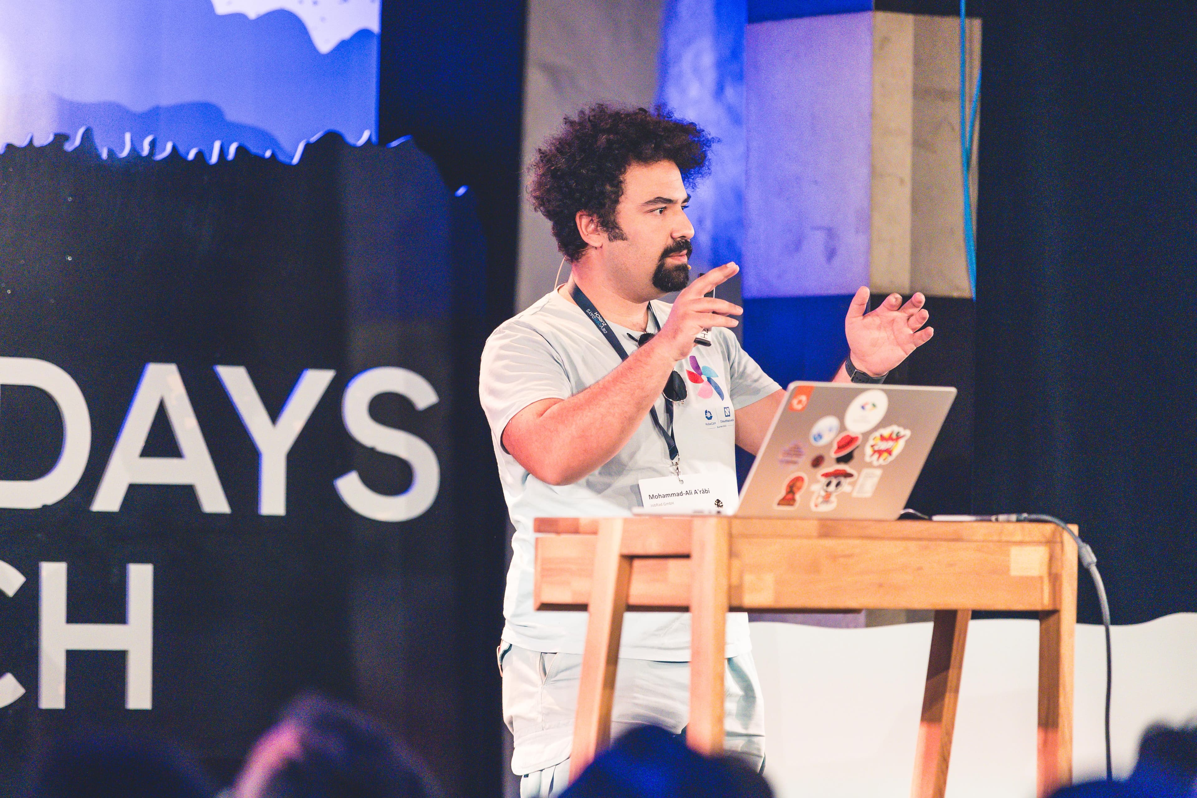 Mohammad-Ali A'râbi presenting on stage at DevOpsDays Zurich 2026.