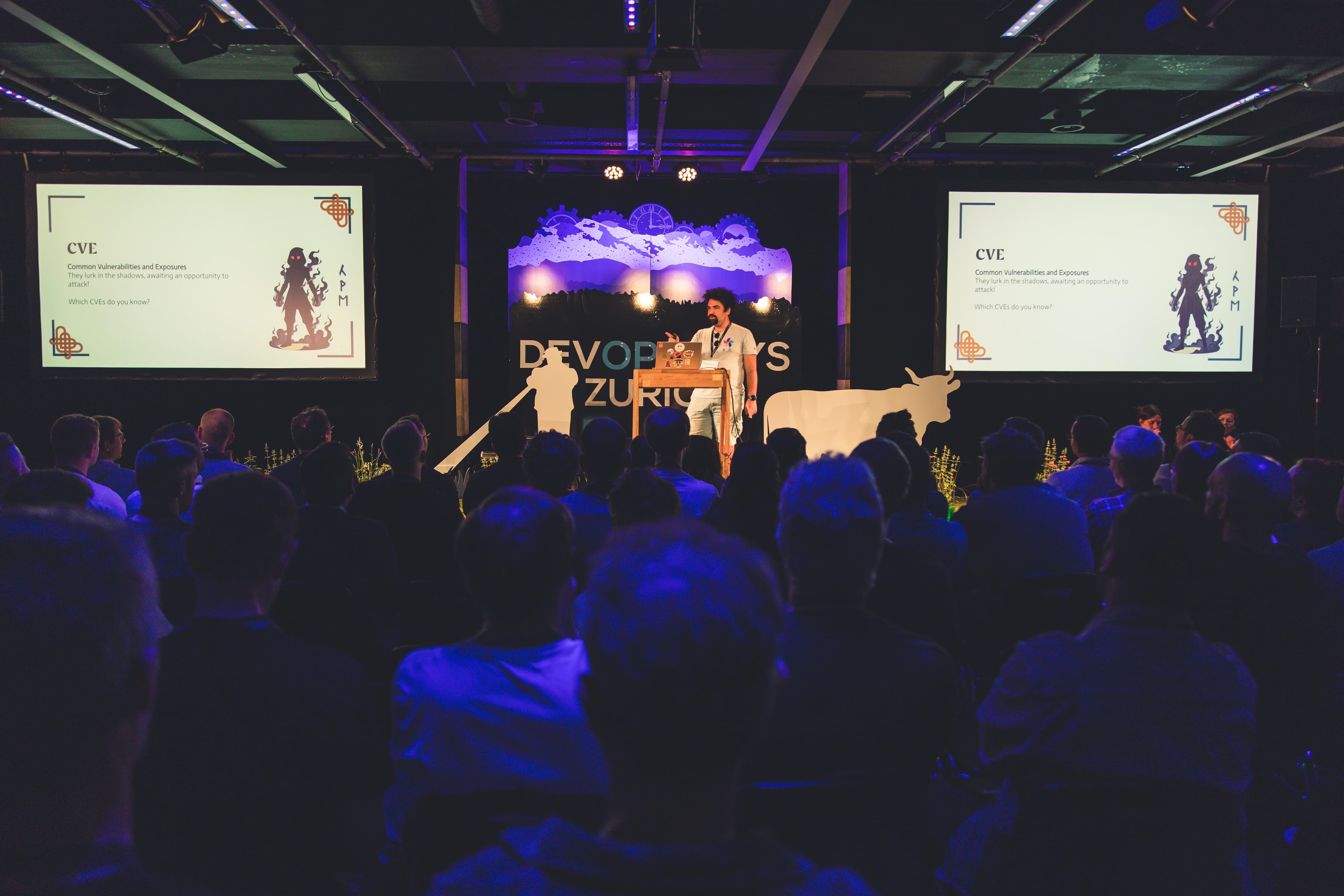Stage and audience view with slides showing CVE content during DevOpsDays Zurich 2026.